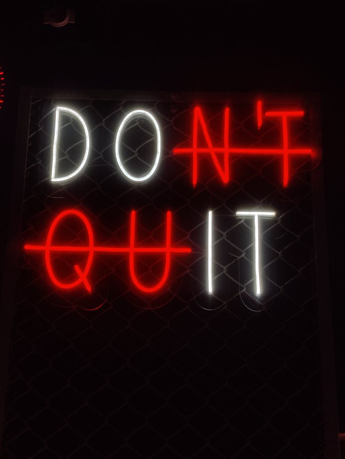 Illuminated 'Don't Quit' neon sign with motivational message in a dark background.